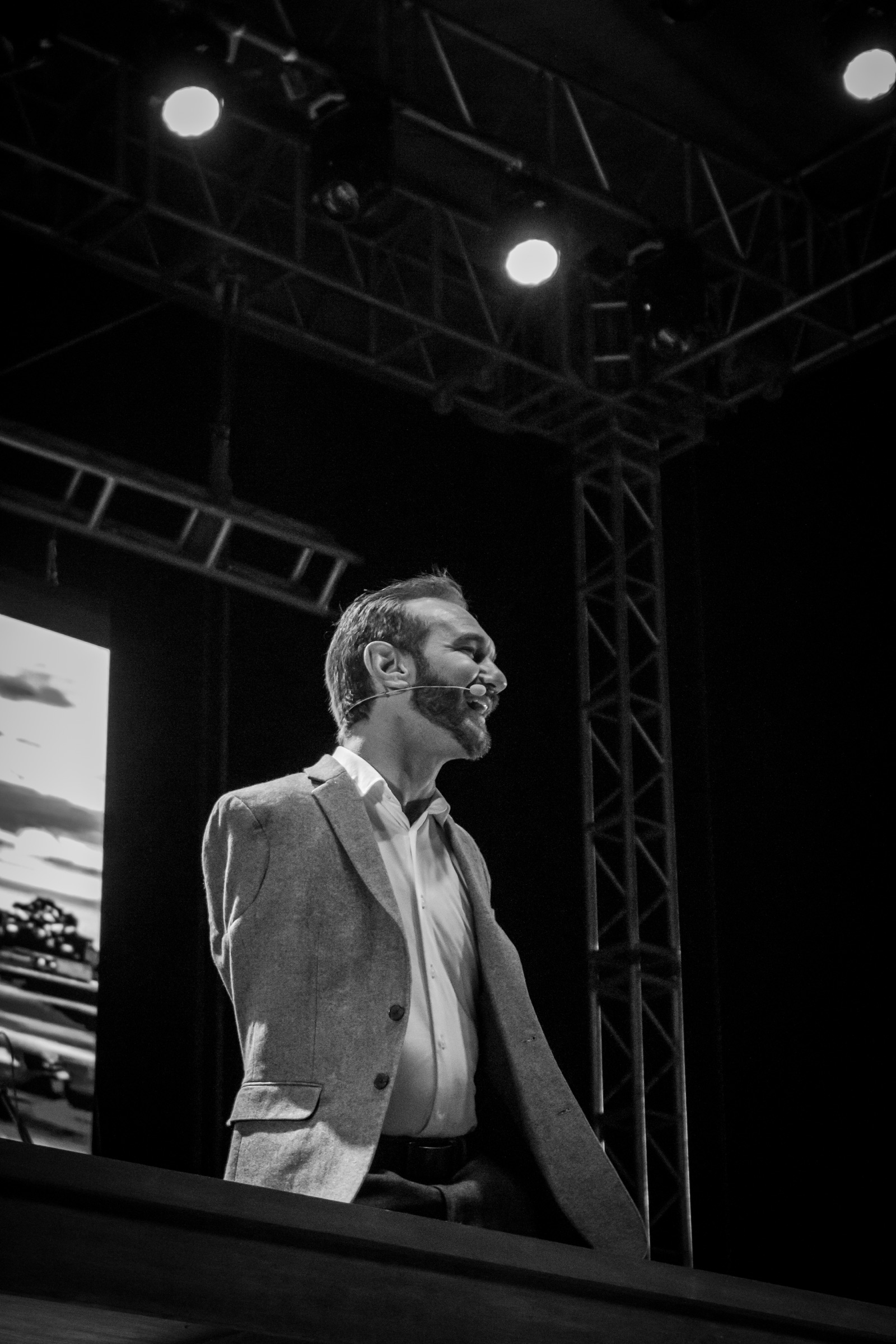 Hombre sonriente hablando sobre un escenario iluminado, en blanco y negro